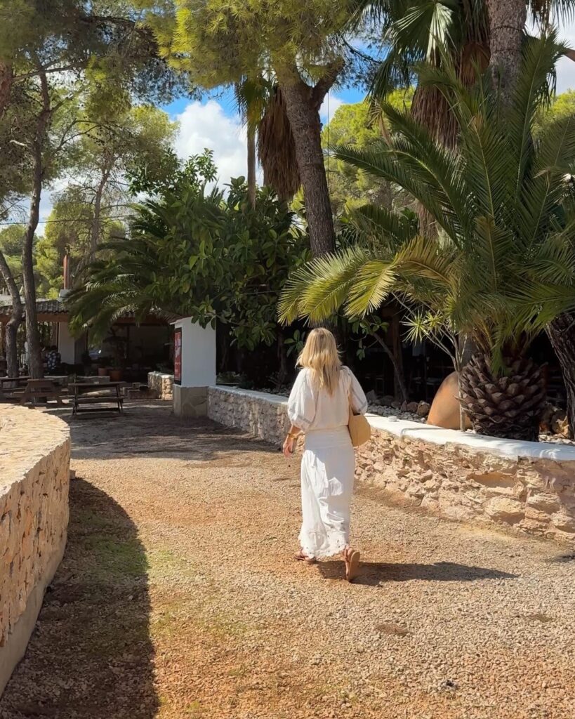What to wear in Ibiza in September: an all-white look walking down a palm-lined path